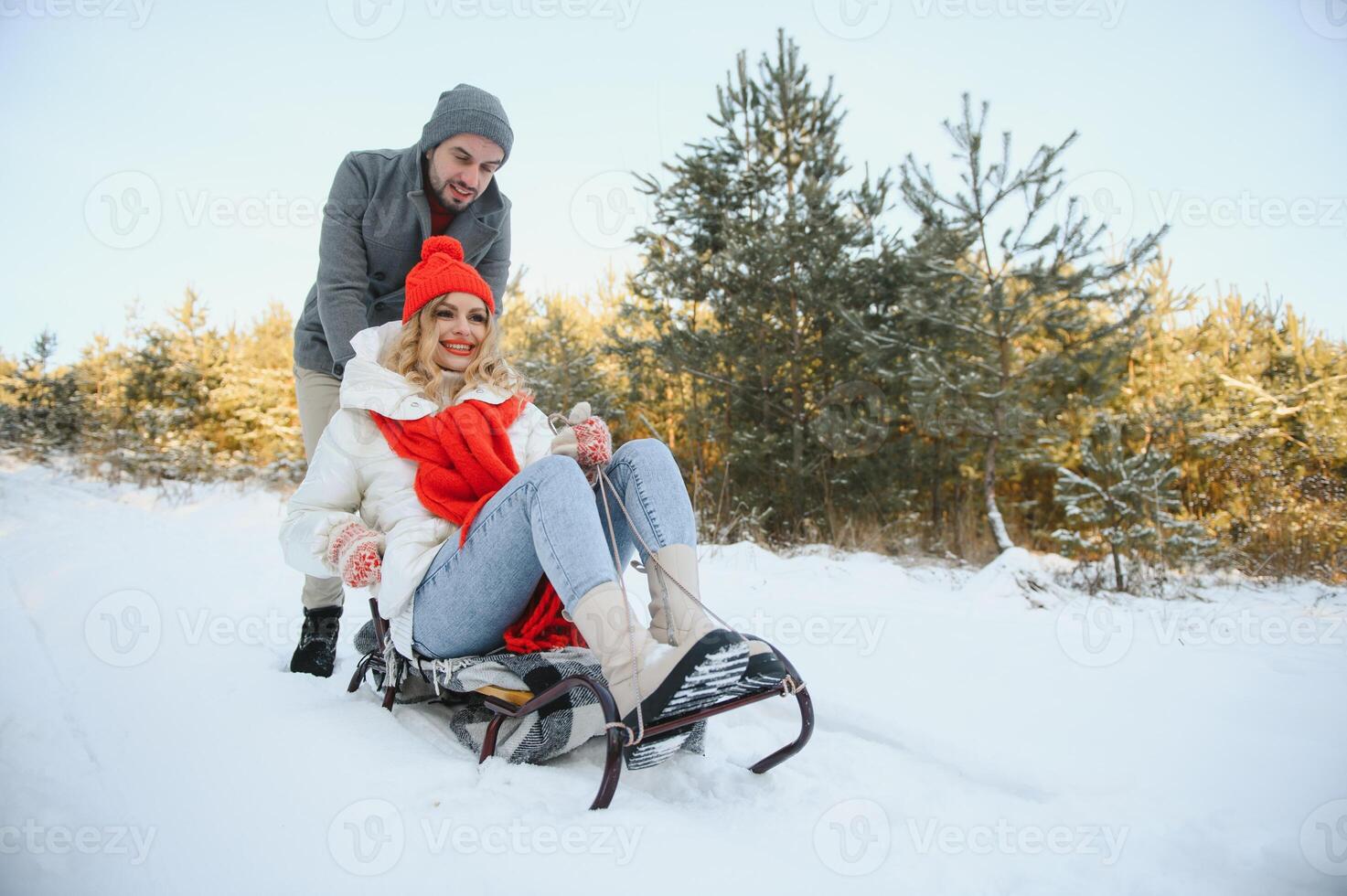 Beautiful young couple in love having fun on a winter vacation in mountains, boyfriend pushing girlfriend on a sled, enjoying snowy, foggy winter day outdoor photo