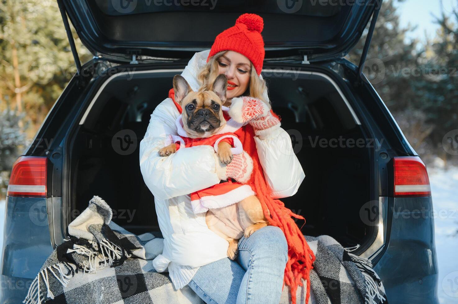 Woman resting in the winter forest sitting in the open trunk of a car with a dog. photo