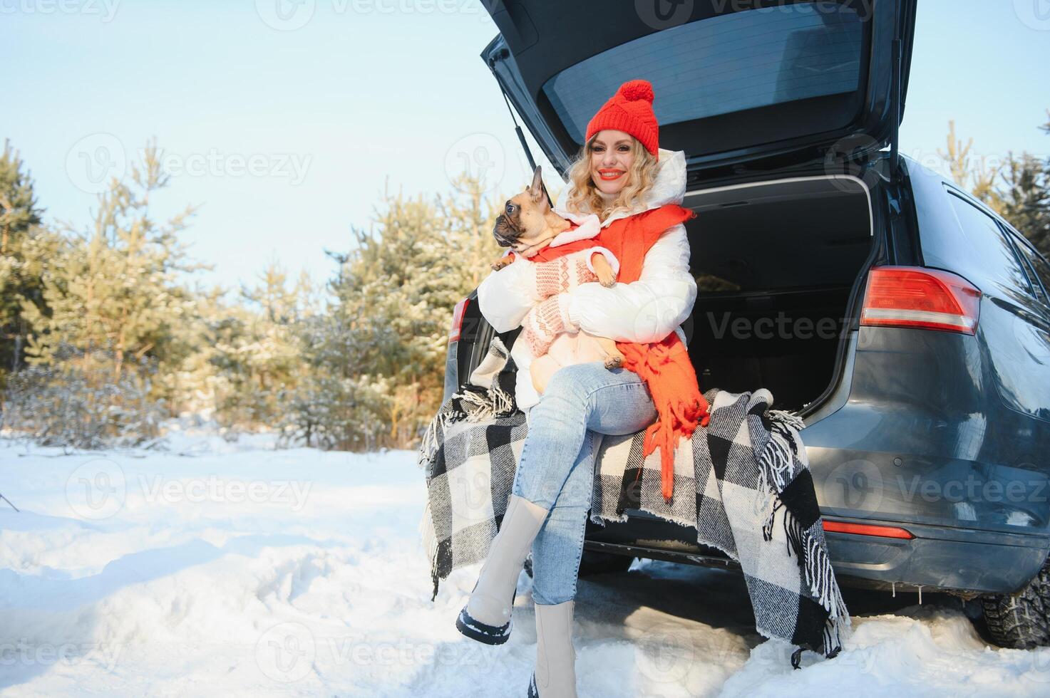 Woman resting in the winter forest sitting in the open trunk of a car with a dog. photo