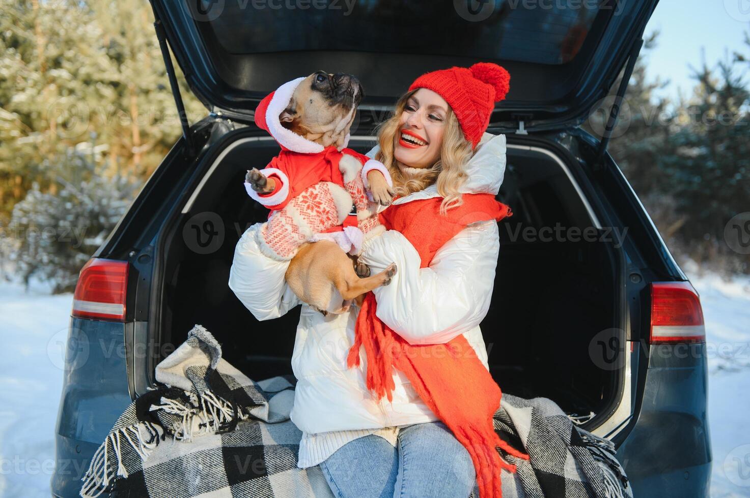 Woman resting in the winter forest sitting in the open trunk of a car with a dog. photo