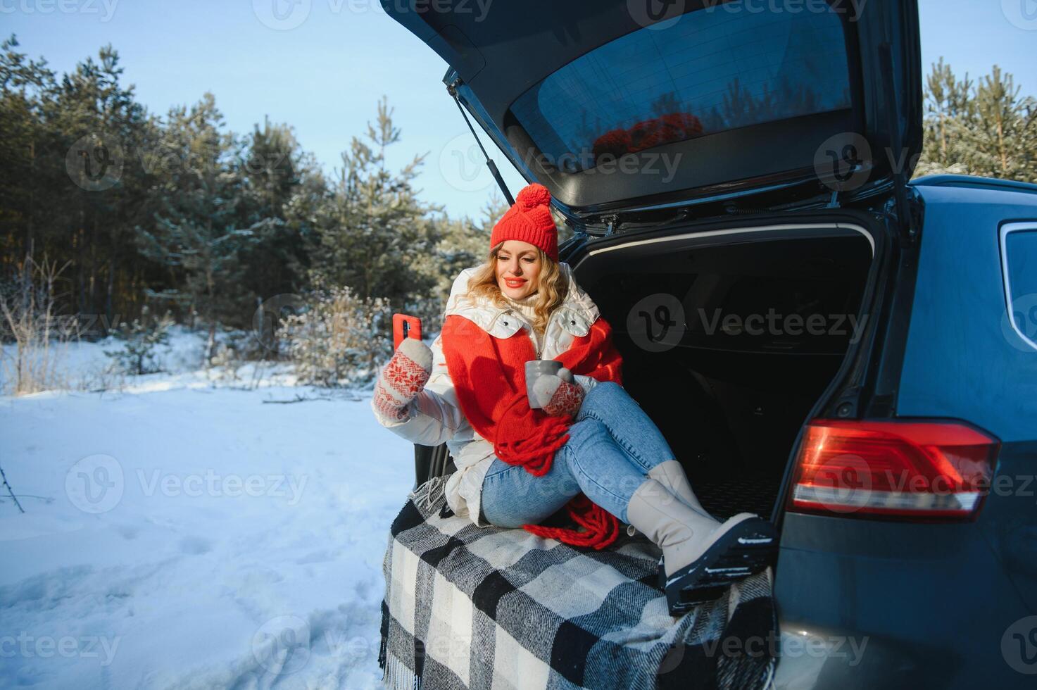 young woman sitting in car trunk drinking warm tea and takes a selfie at winter snowed day. photo