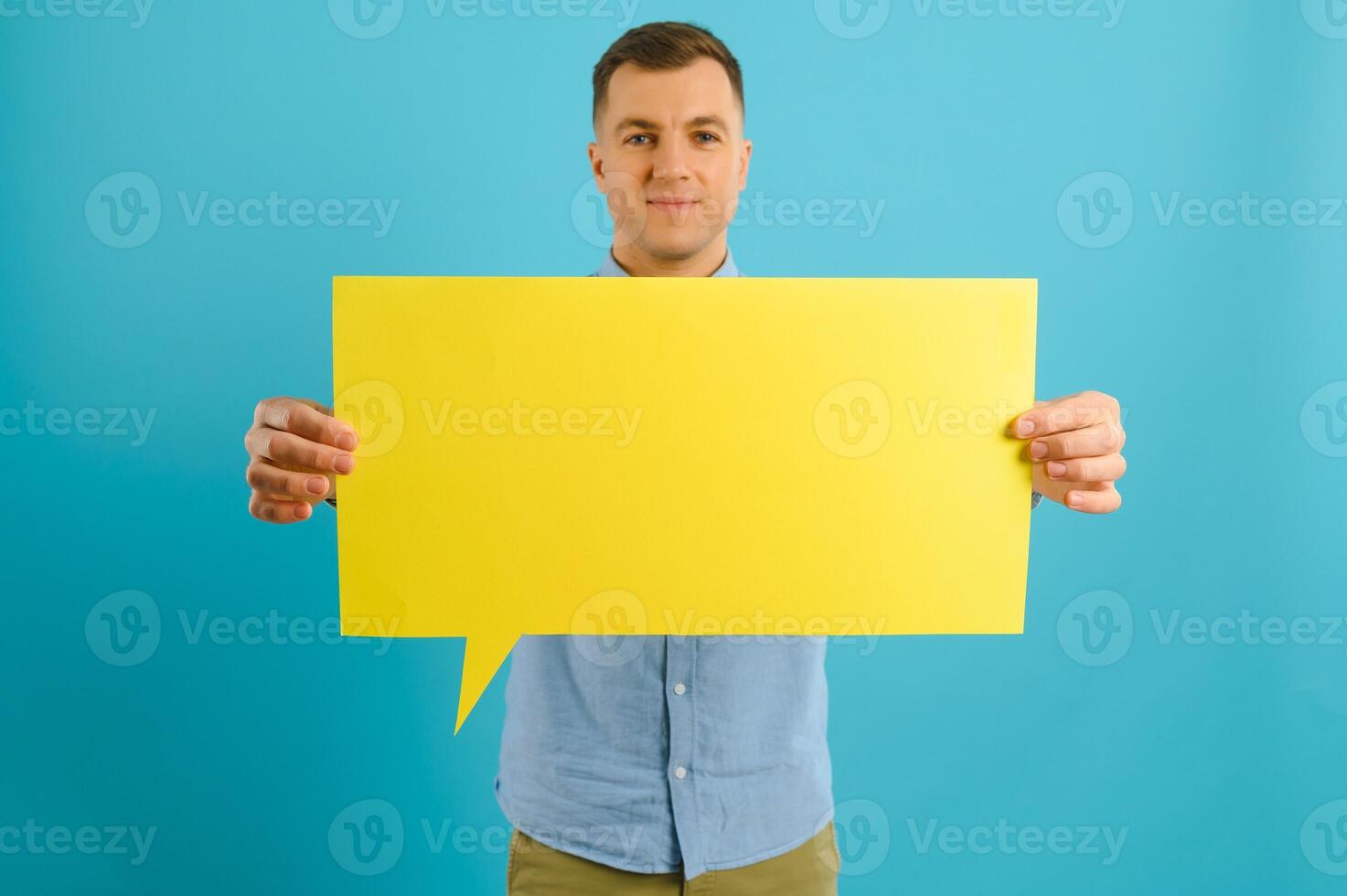 Joyful Caucasian man demonstrating blank placard on blue studio background, mockup for design photo