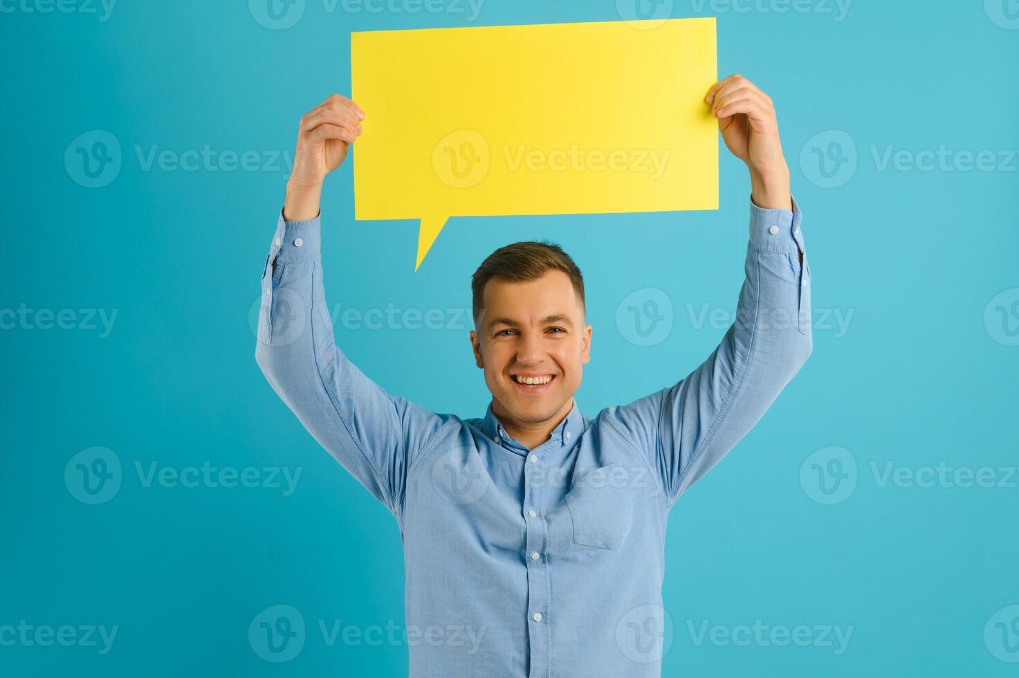 Joyful Caucasian man demonstrating blank placard on blue studio background, mockup for design photo