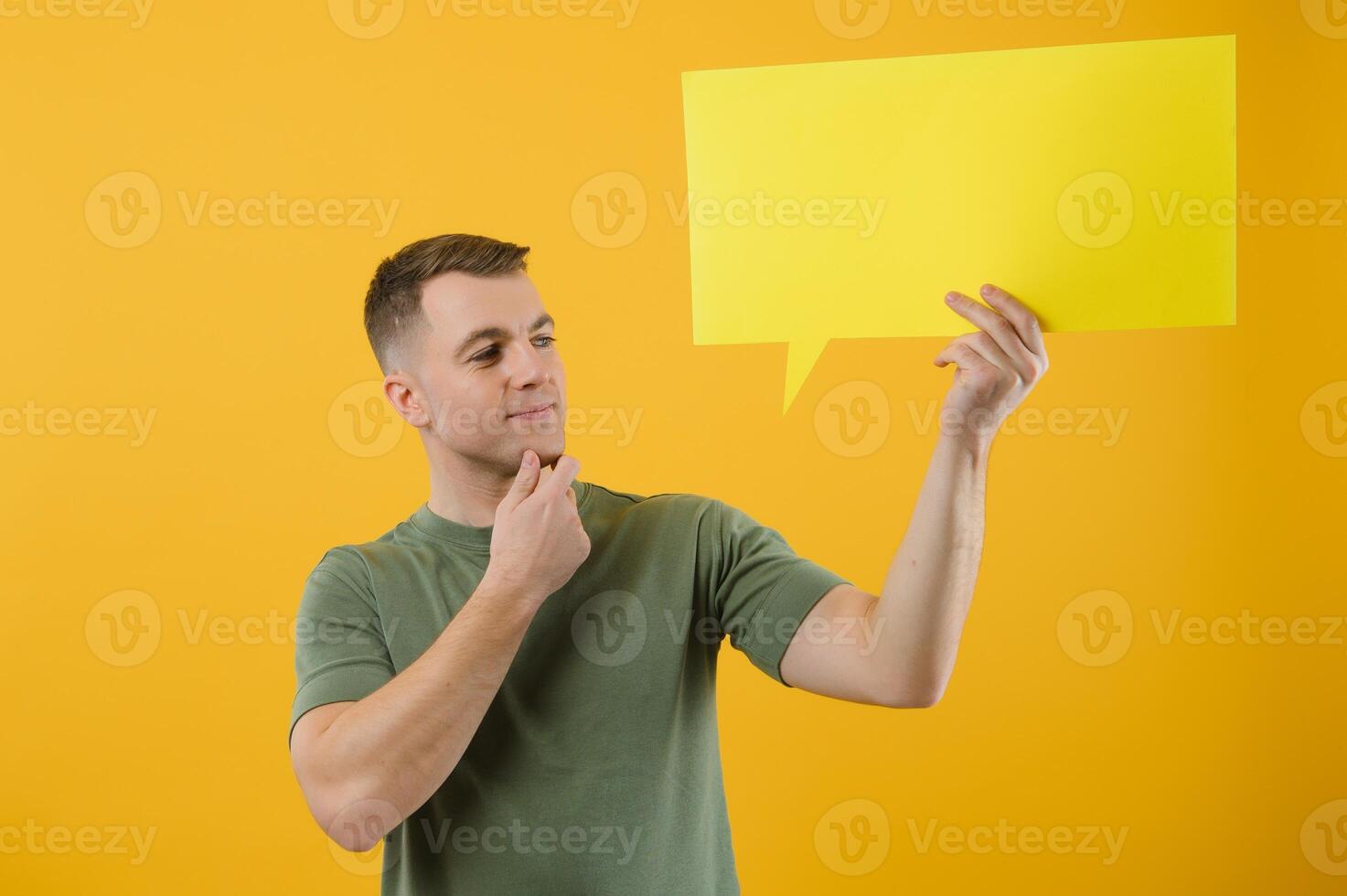 Cheerful young male pointing up and holding empty speech bubble with blank space for quote against vivid yellow background photo