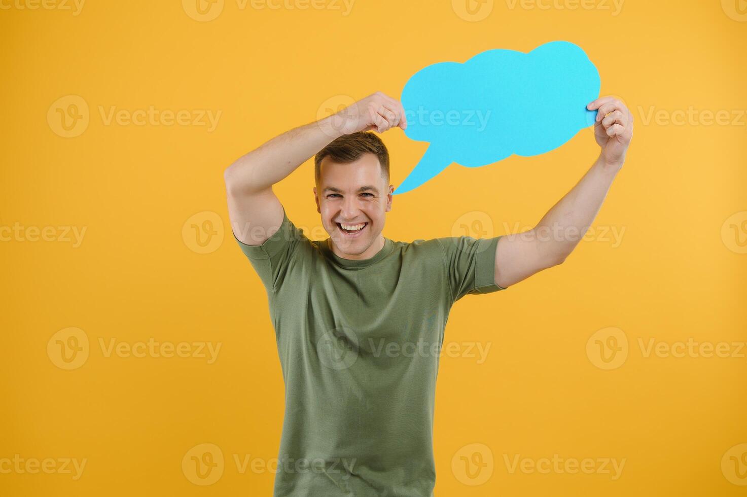 Happy guy smiling and holding blank speech balloon near head against yellow background photo