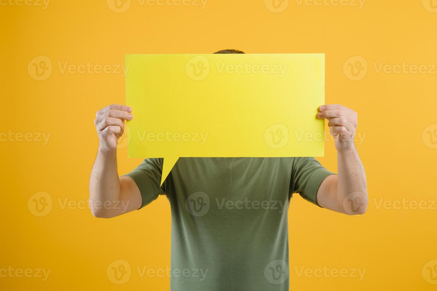 Cheerful young male pointing up and holding empty speech bubble with blank space for quote against vivid yellow background photo
