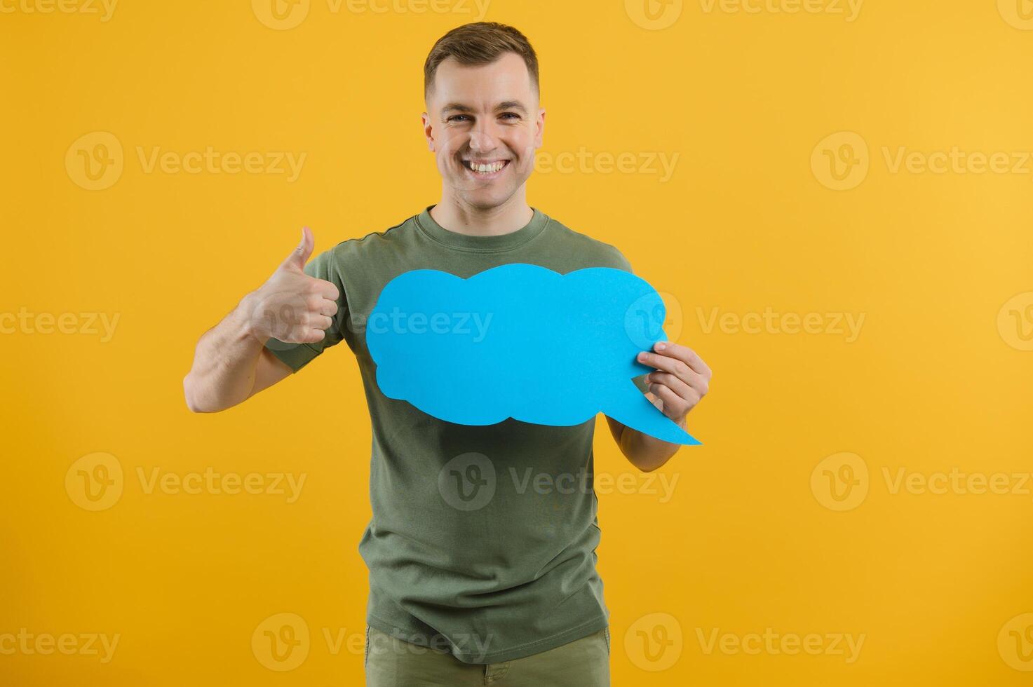 Cheerful young male pointing up and holding empty speech bubble with blank space for quote against vivid yellow background photo