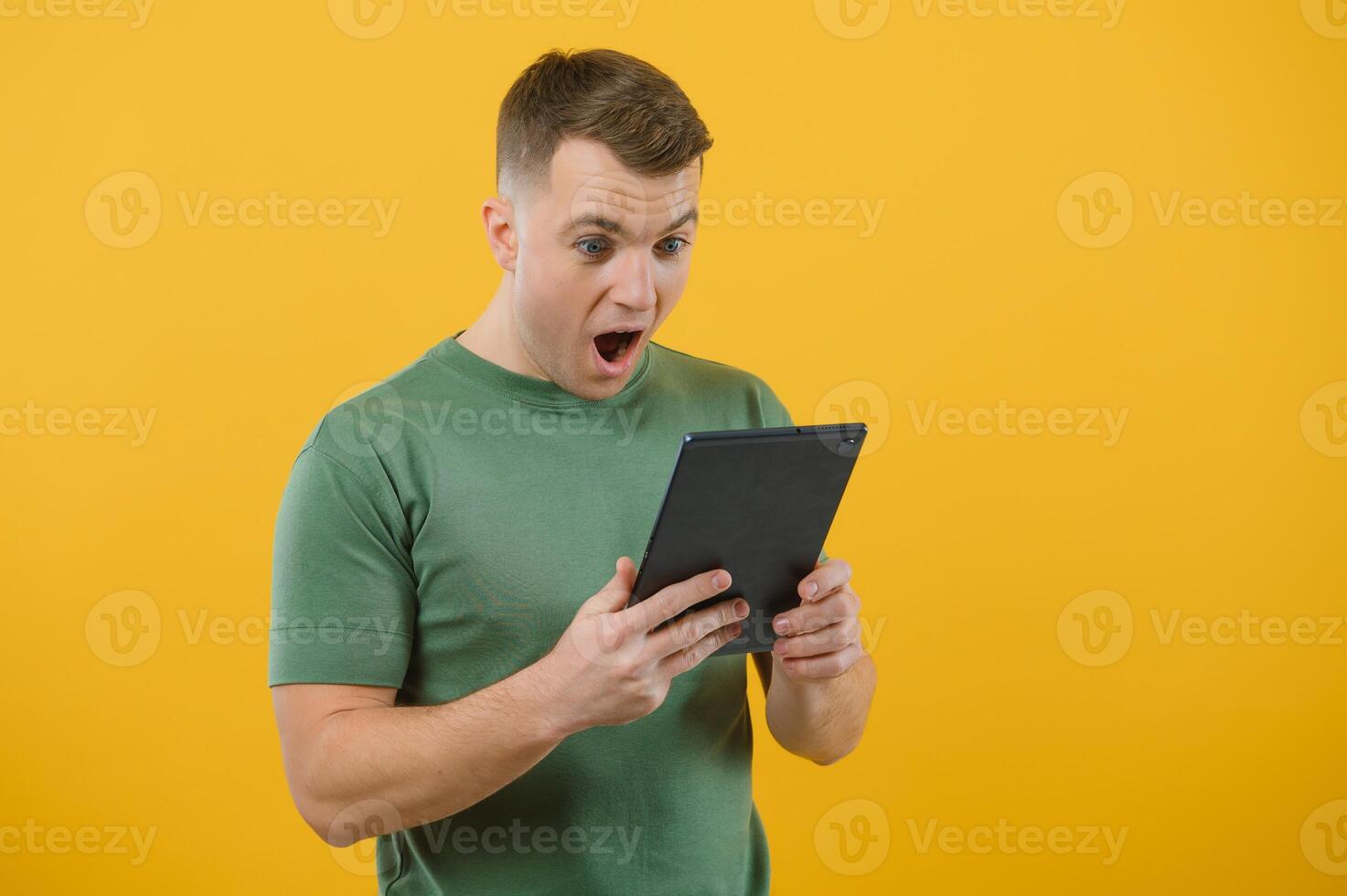 Amazed happy man using digital tablet looking shocked about social media news, astonished man shopper consumer surprised excited by online win isolated over yellow background. photo