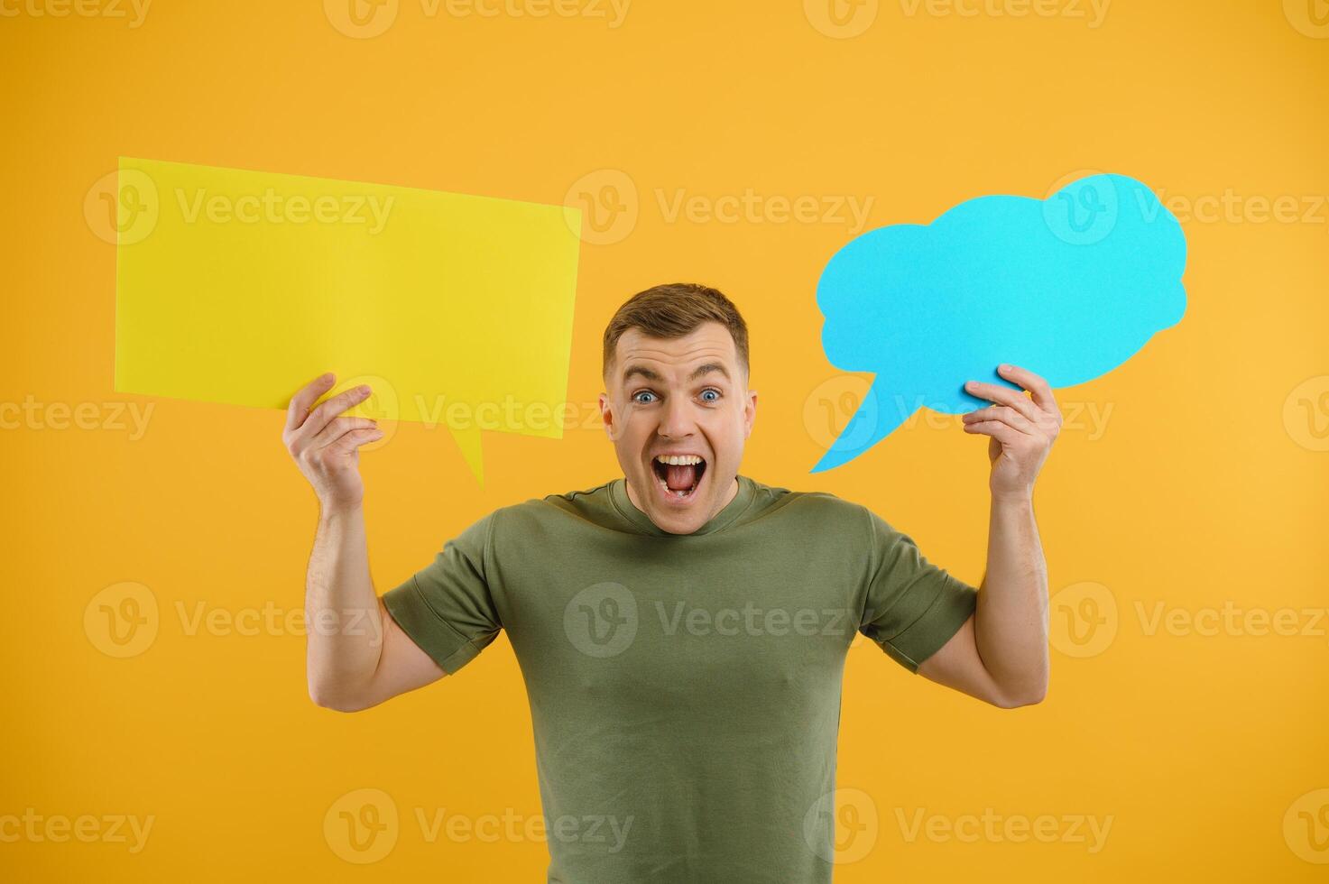Portrait of cheerful smiling young handsome man holding and looking up at speech bubble with empty space for text on colorful yellow studio background photo