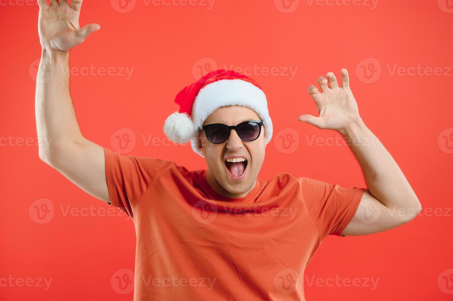 Portrait of happy and excited man in santa hat, rejoicing and winning something, celebrating new year, standing over red background photo