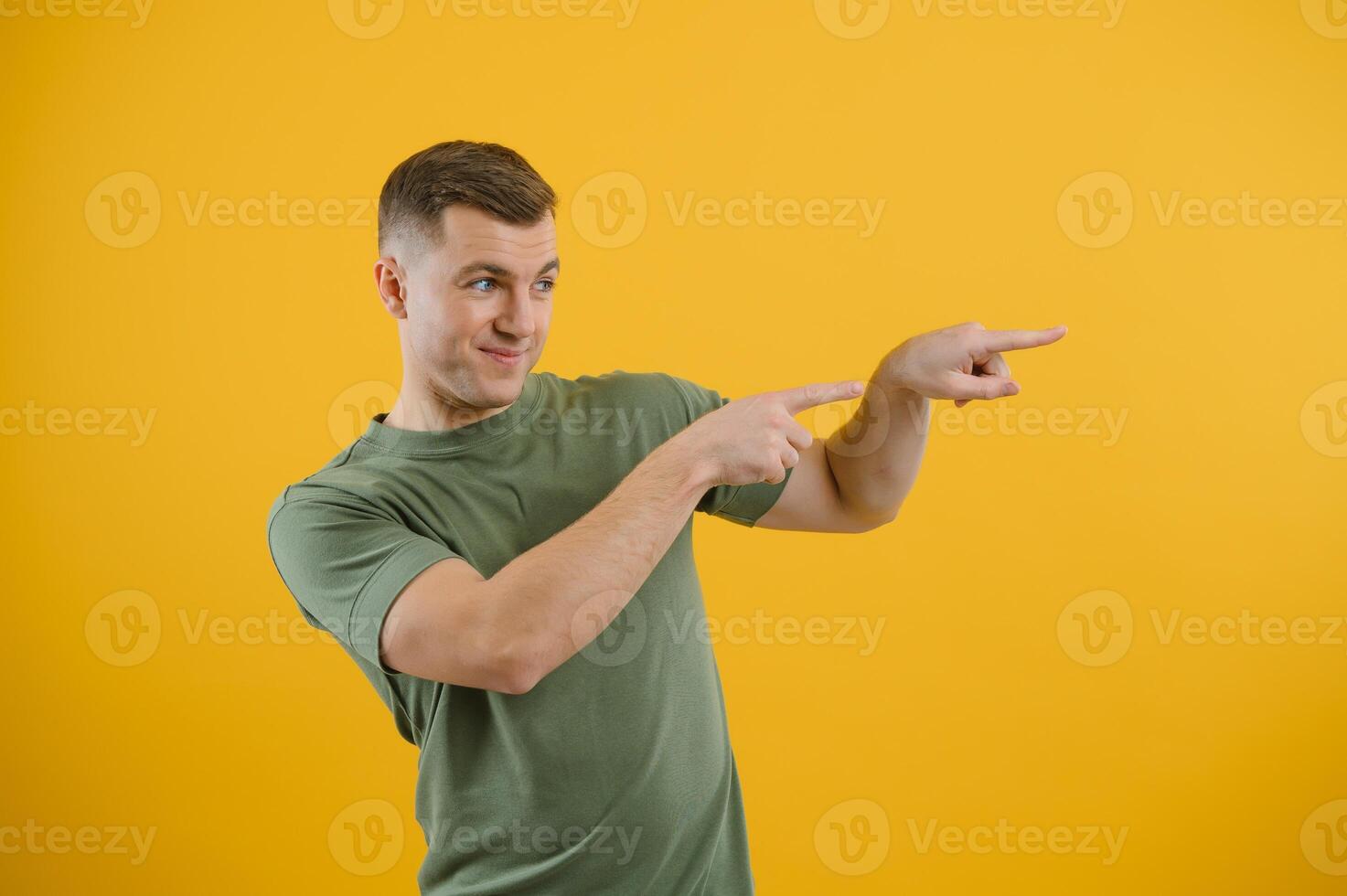 Portrait of a joyful young man pointing fingers away at copy space on his palm isolated over yellow background photo