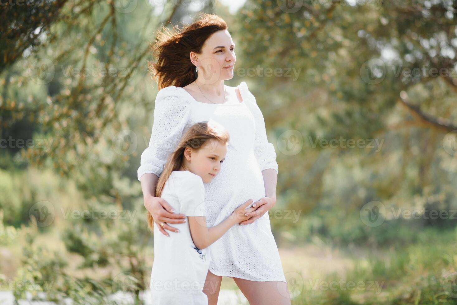 Pregnant woman and her daughter in the park at sunset. A happy family. photo