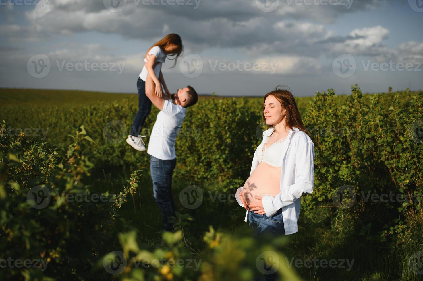 Happy family. Dad, pregnant mom and little daughter play games at sunset in summer in park. photo