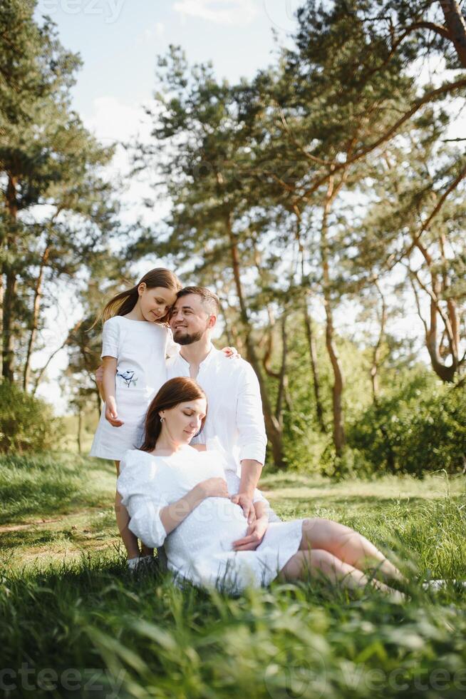 Happy pregnant couple with daughter in summer nature. photo