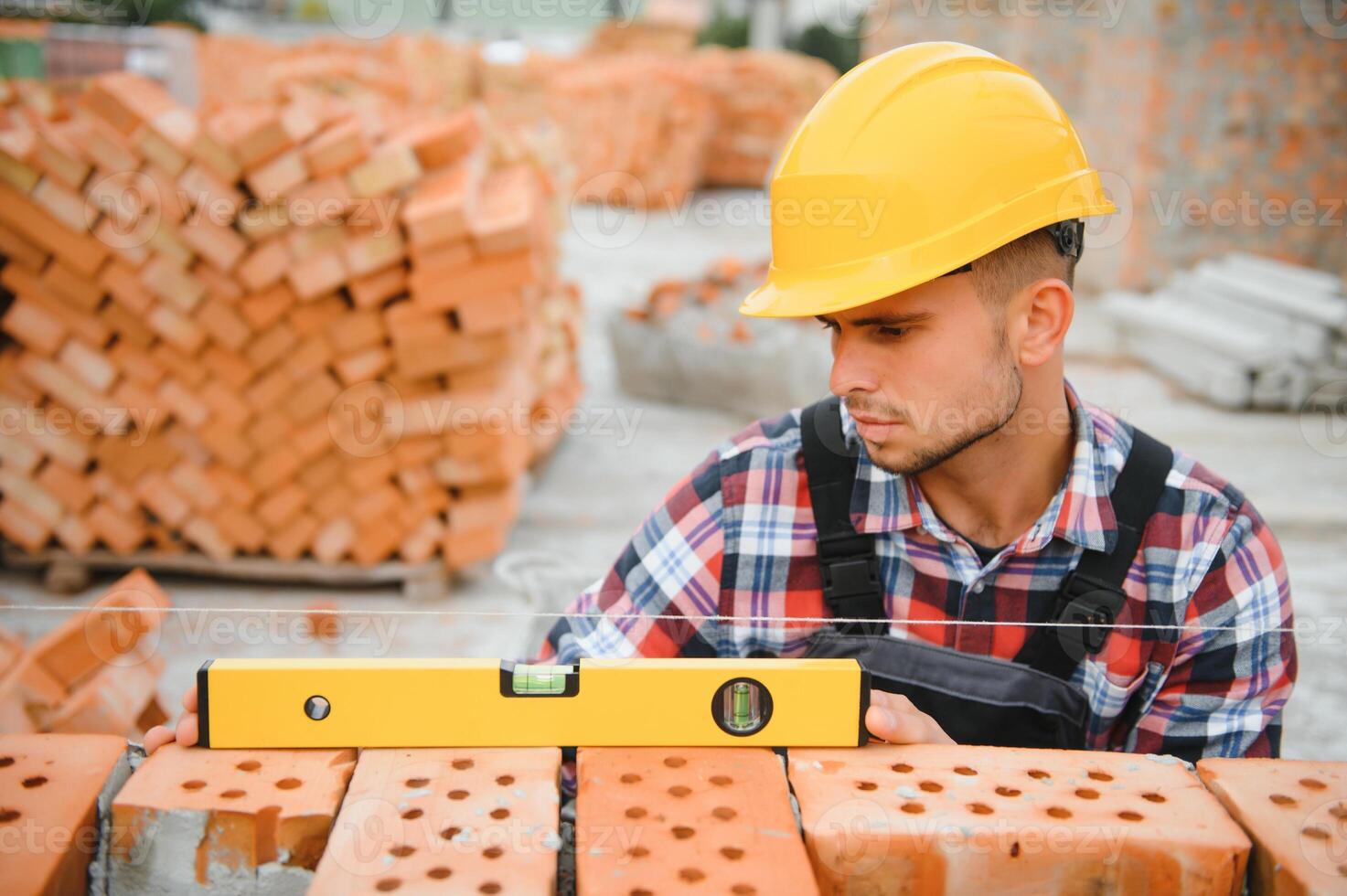 Using bricks. Young construction worker in uniform is busy at the unfinished building photo