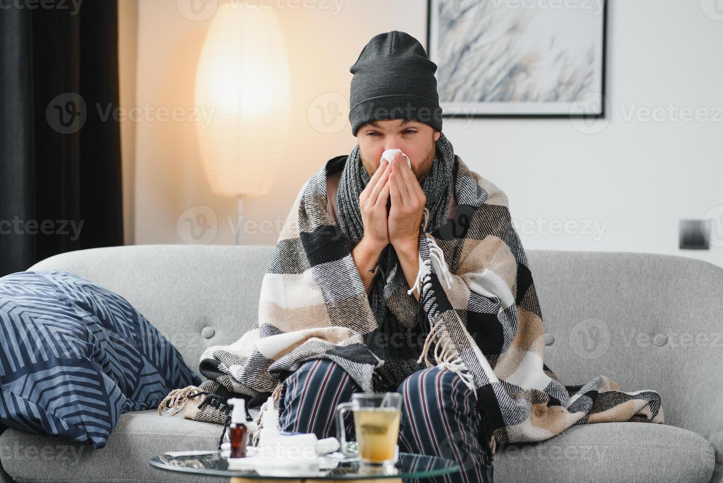 Sick man on sofa at home and blowing nose photo