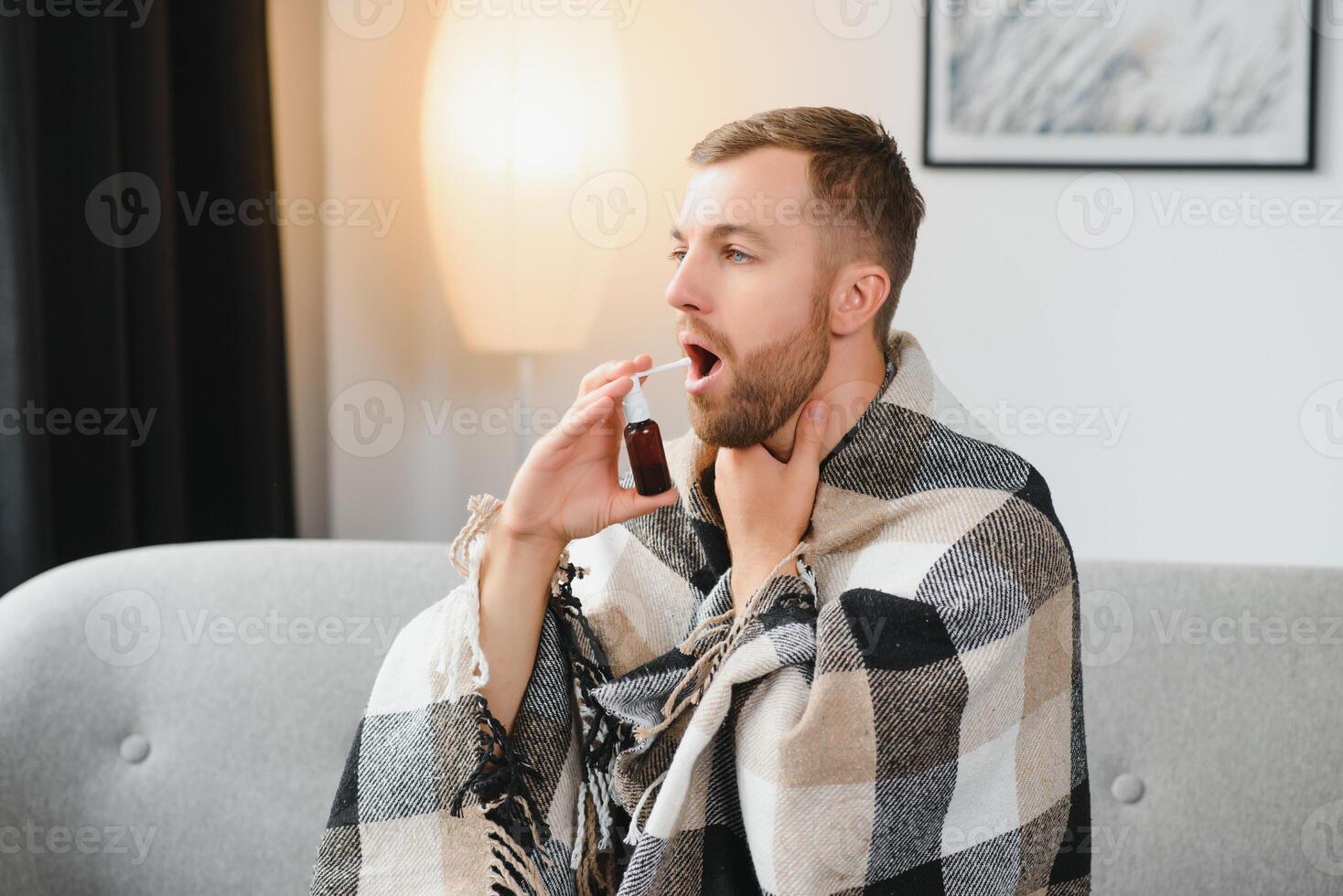 rhinitis, medicine and healthcare concept - sick man in blanket using oral spray at home photo