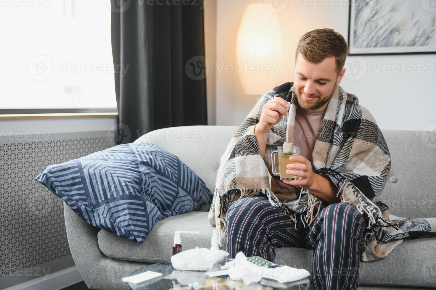 Young man suffering from cold at his home. Shot of a young man sitting on his bed while feeling unwell at home. Trying to stay warm. Sick man photo