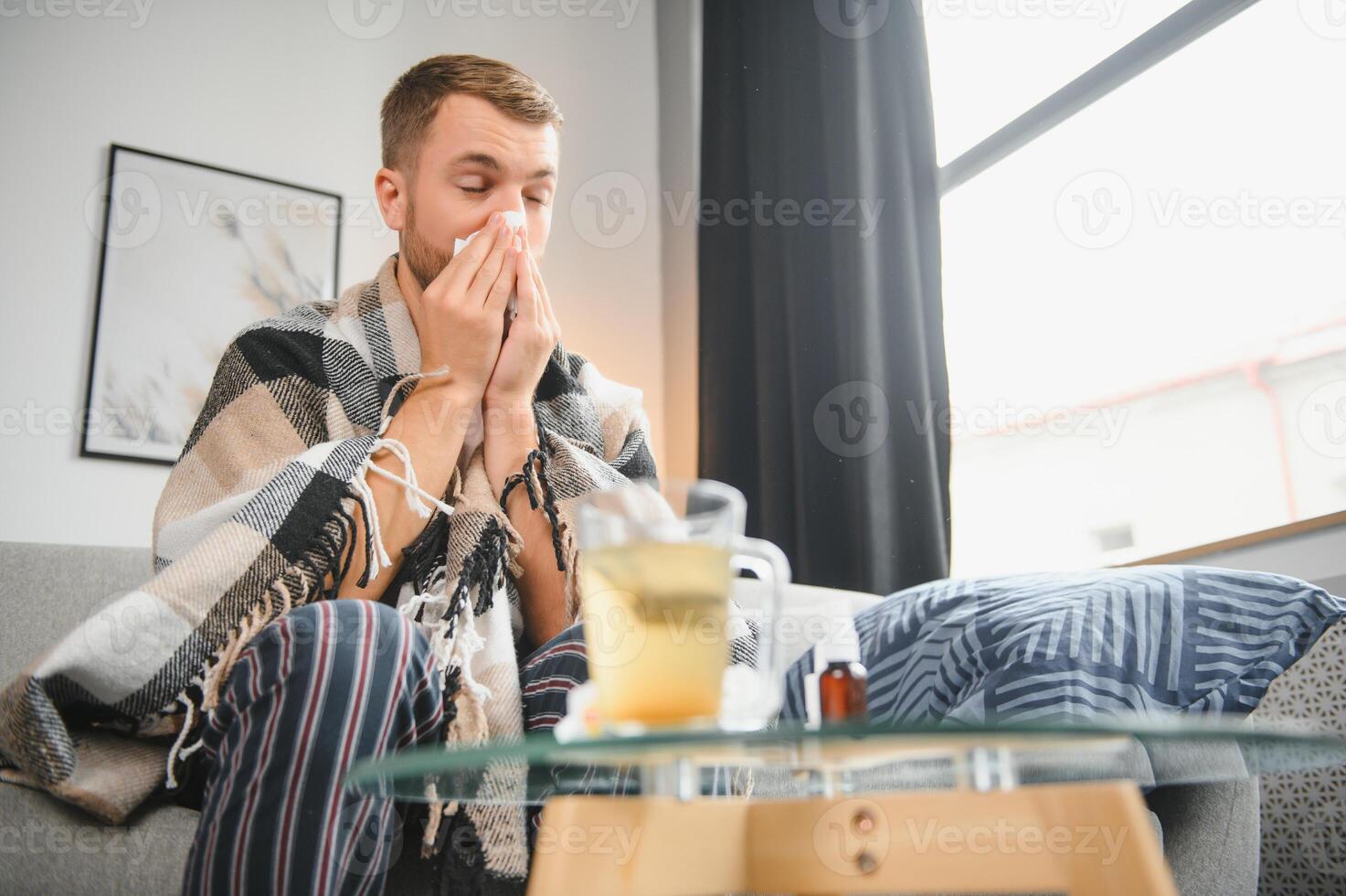Sick man on sofa at home and blowing nose photo