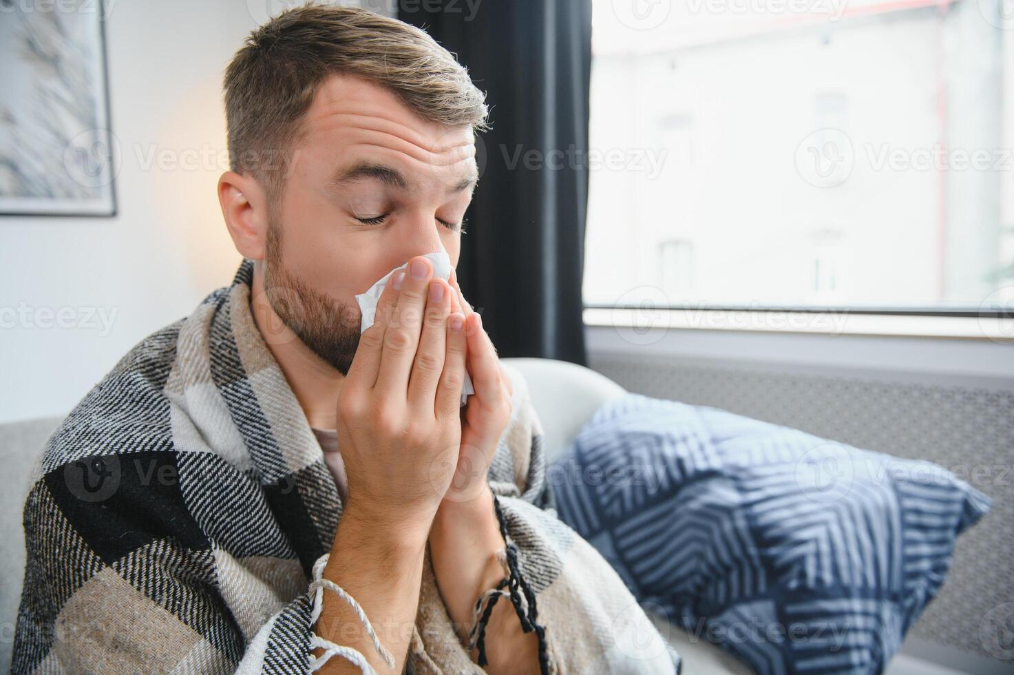 Sick man on sofa at home and blowing nose photo