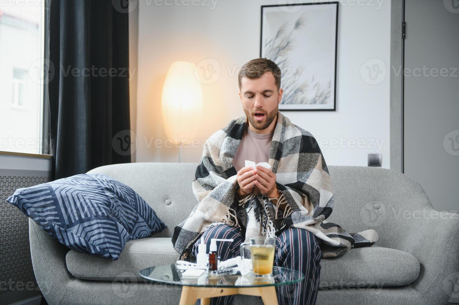 A sick man sits at home on a gray sofa with a blanket. Illness, protection, coronavirus, illness, flu photo