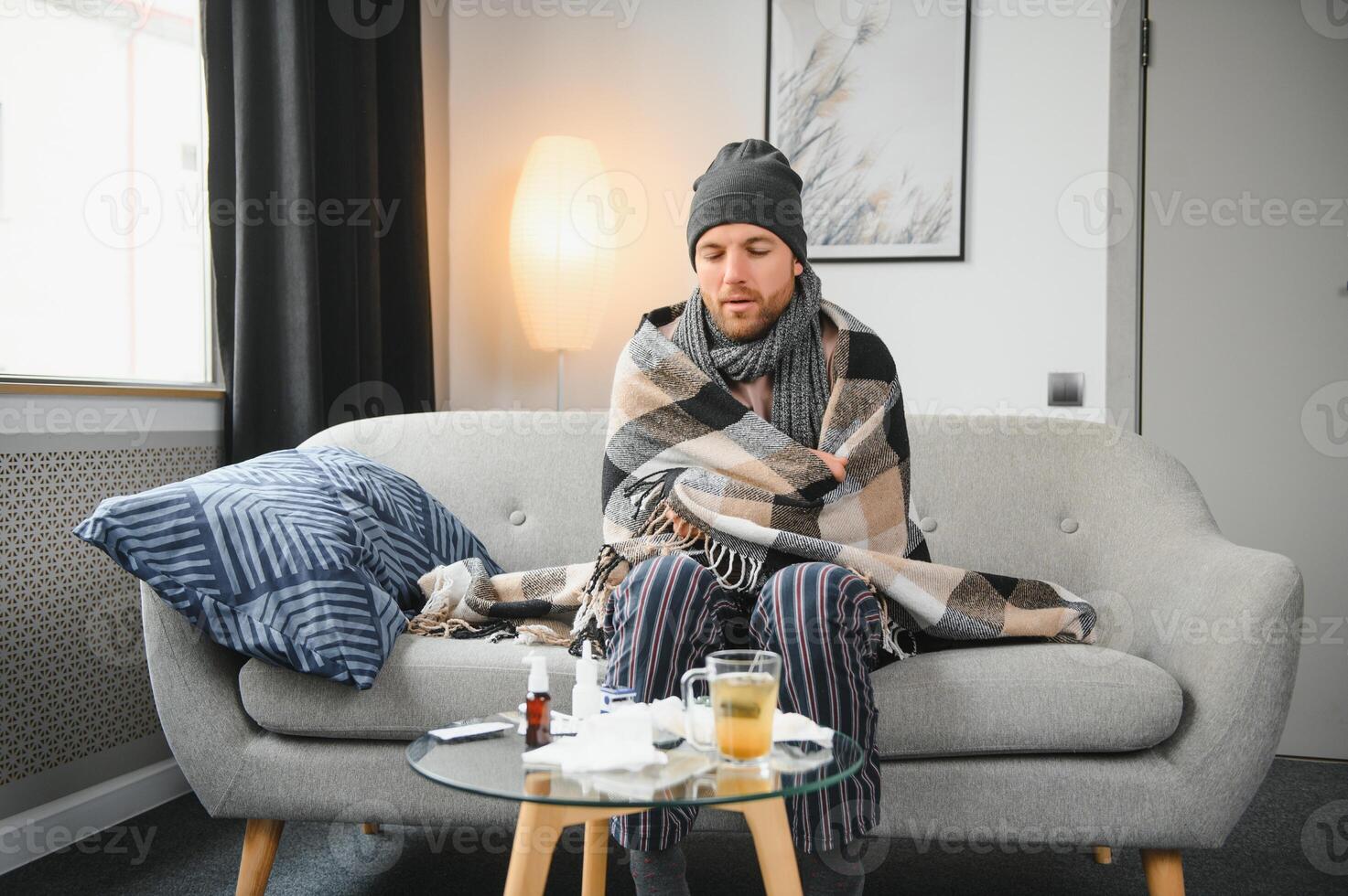A sick man sits at home on a gray sofa with a blanket. Illness, protection, coronavirus, illness, flu photo