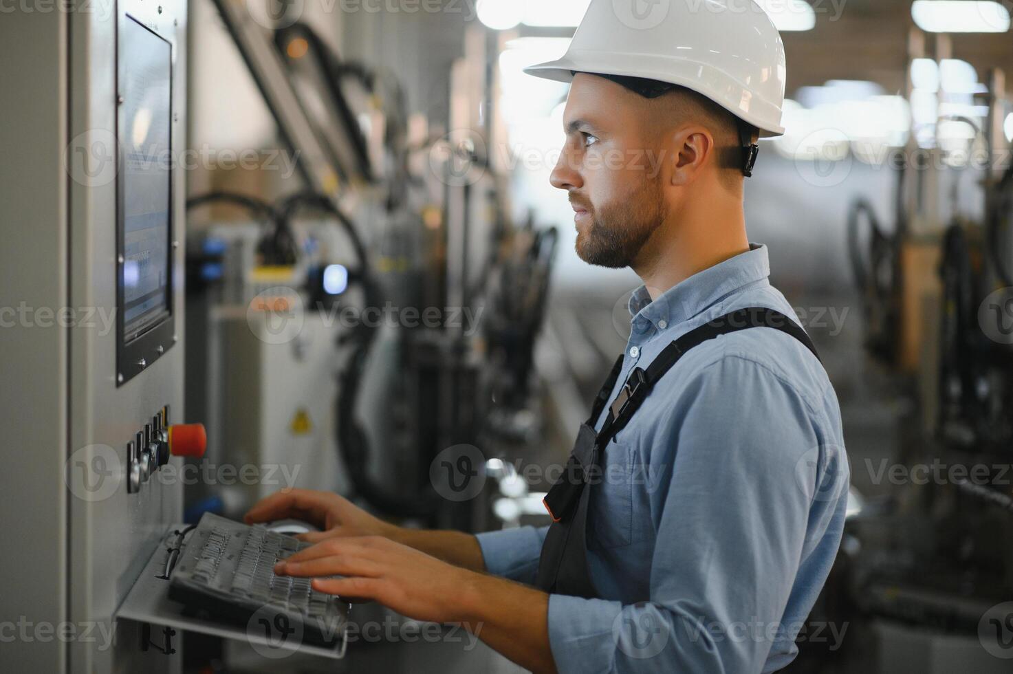 Portrait of factory worker in protective uniform and hardhat standing by industrial machine at production line. People working in industry photo