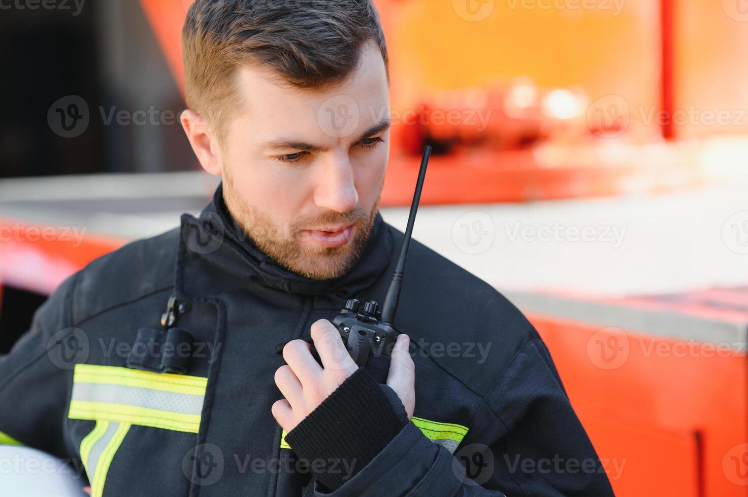 Fireman in a protective uniform standing next to a fire truck and talking on the radio. photo