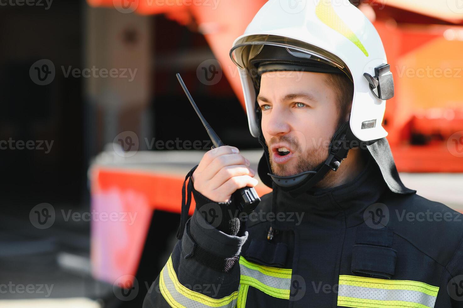Fireman in a protective uniform standing next to a fire truck and talking on the radio. photo