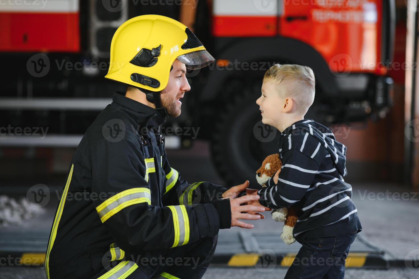 Dirty firefighter in uniform holding little saved boy standing on black background. photo