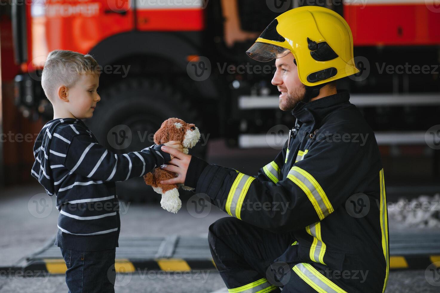 Dirty firefighter in uniform holding little saved boy standing on black background. photo
