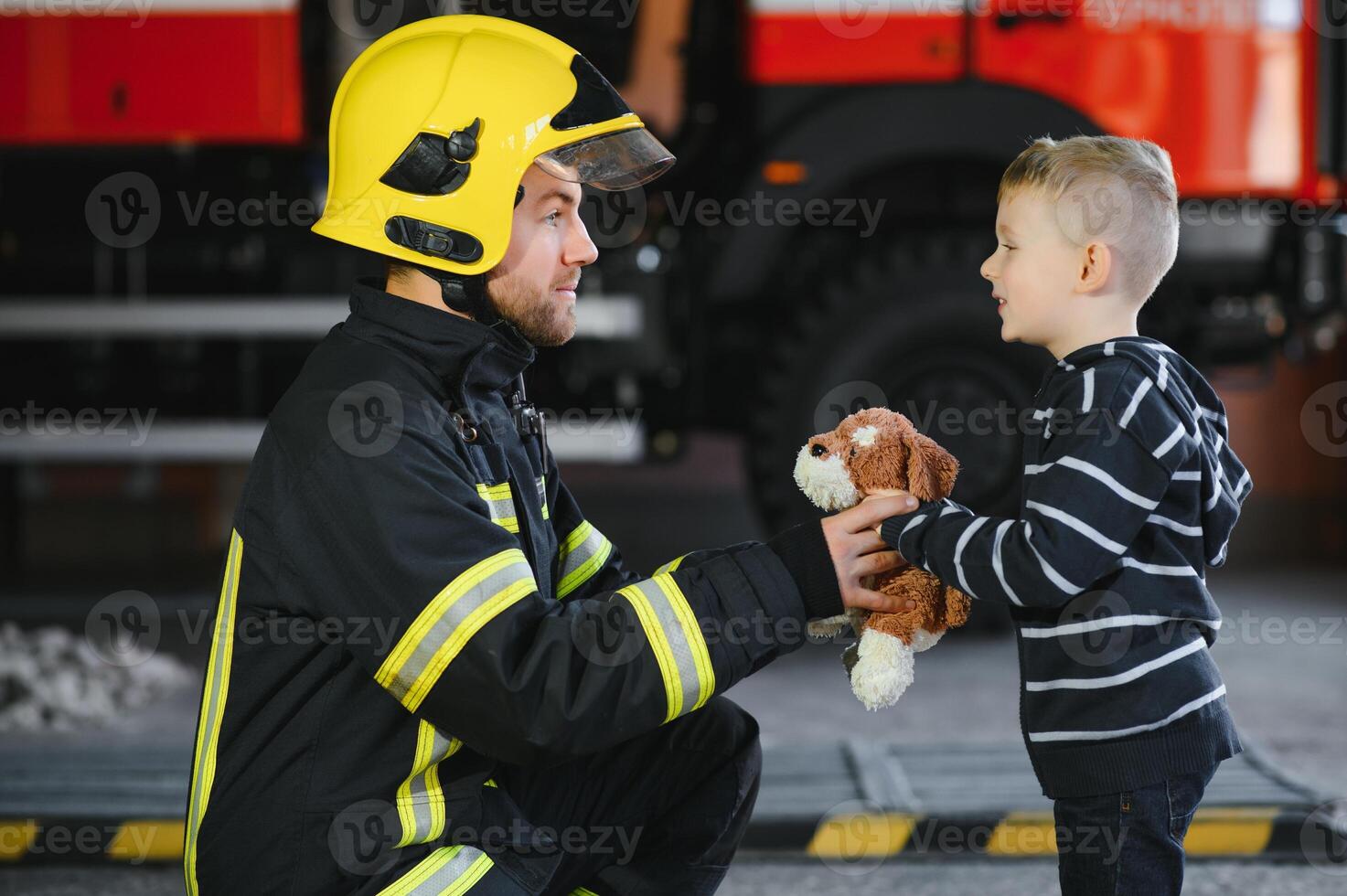 A firefighter take a little child boy to save him. Fire engine car on background. Fireman with kid in his arms. Protection concept. photo