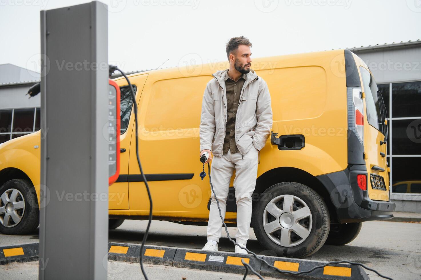 Portrait of a young man standing with charging cable near the charging station photo