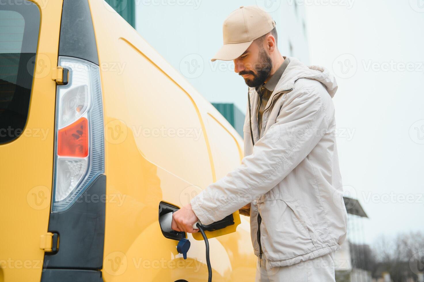 Portrait of a young man standing with charging cable near the charging station photo