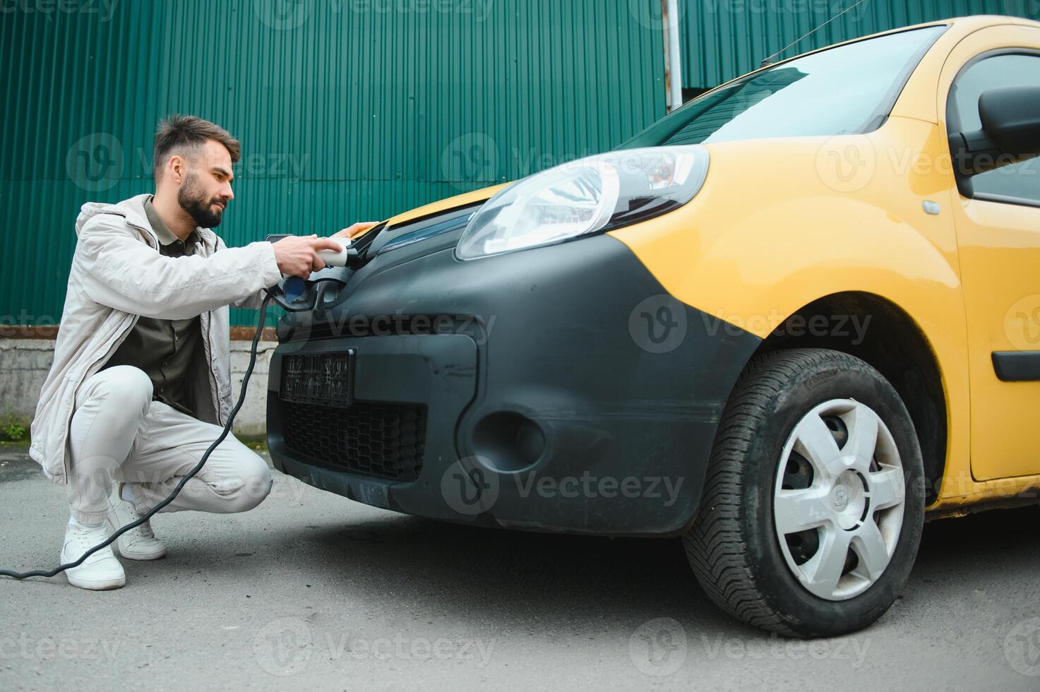 Man Holding Power Charging Cable For Electric Car In Outdoor Car Park. And he s going to connect the car to the charging station in the parking lot near the shopping center photo