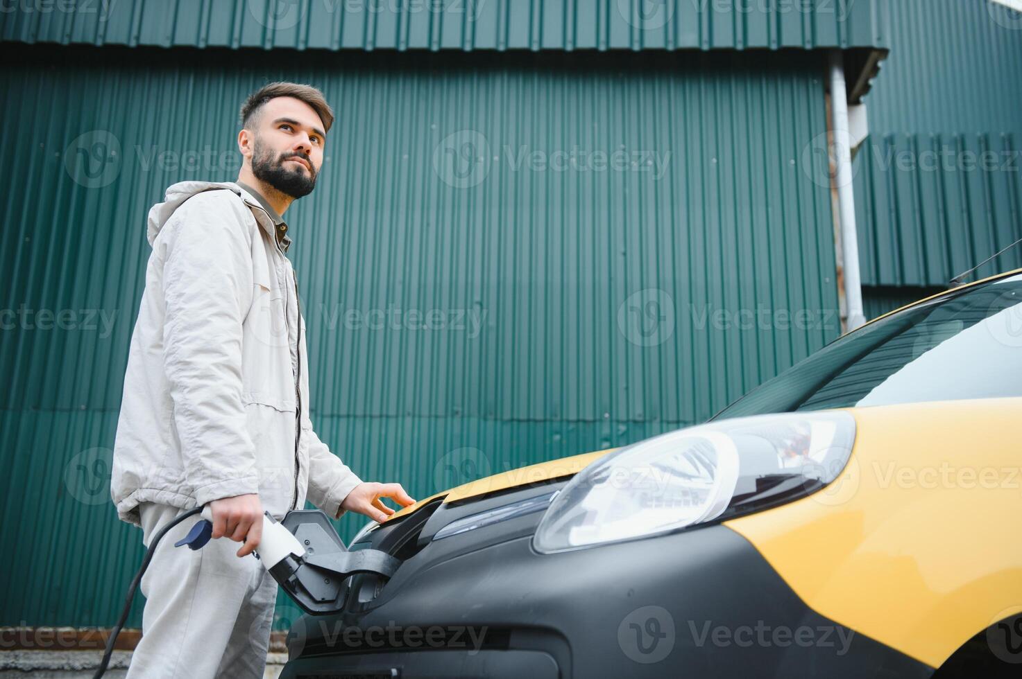 Man Holding Power Charging Cable For Electric Car In Outdoor Car Park. And he s going to connect the car to the charging station in the parking lot near the shopping center photo