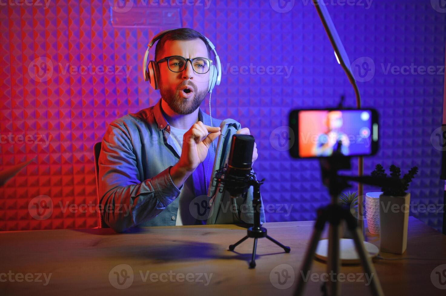vlogger using smartphone to film podcast in studio. blogger with mobile phone, microphone and headphones filming for social media broadcasting career. photo