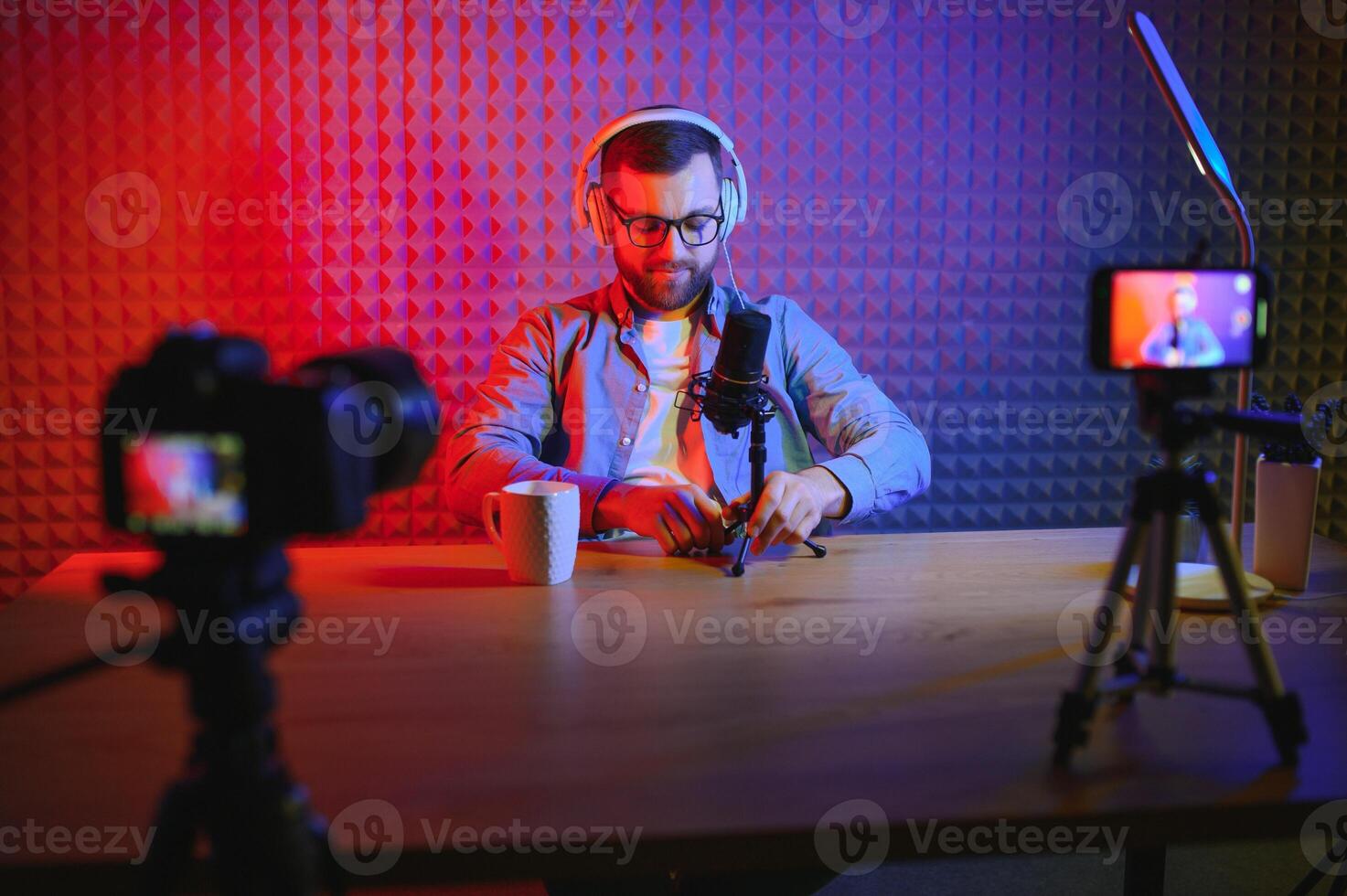 vlogger using smartphone to film podcast in studio. blogger with mobile phone, microphone and headphones filming for social media broadcasting career. photo