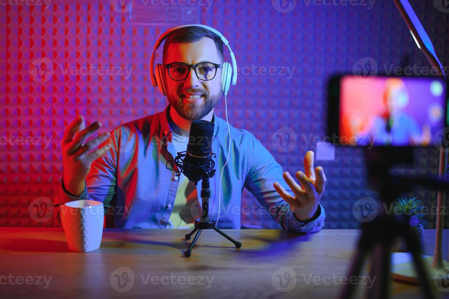 vlogger using smartphone to film podcast in studio. blogger with mobile phone, microphone and headphones filming for social media broadcasting career. photo