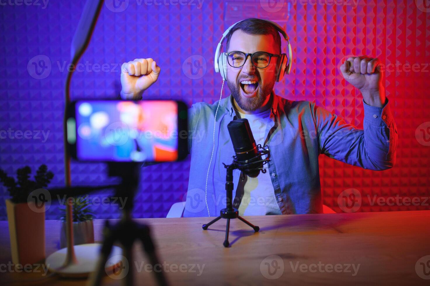 vlogger using smartphone to film podcast in studio. blogger with mobile phone, microphone and headphones filming for social media broadcasting career. photo