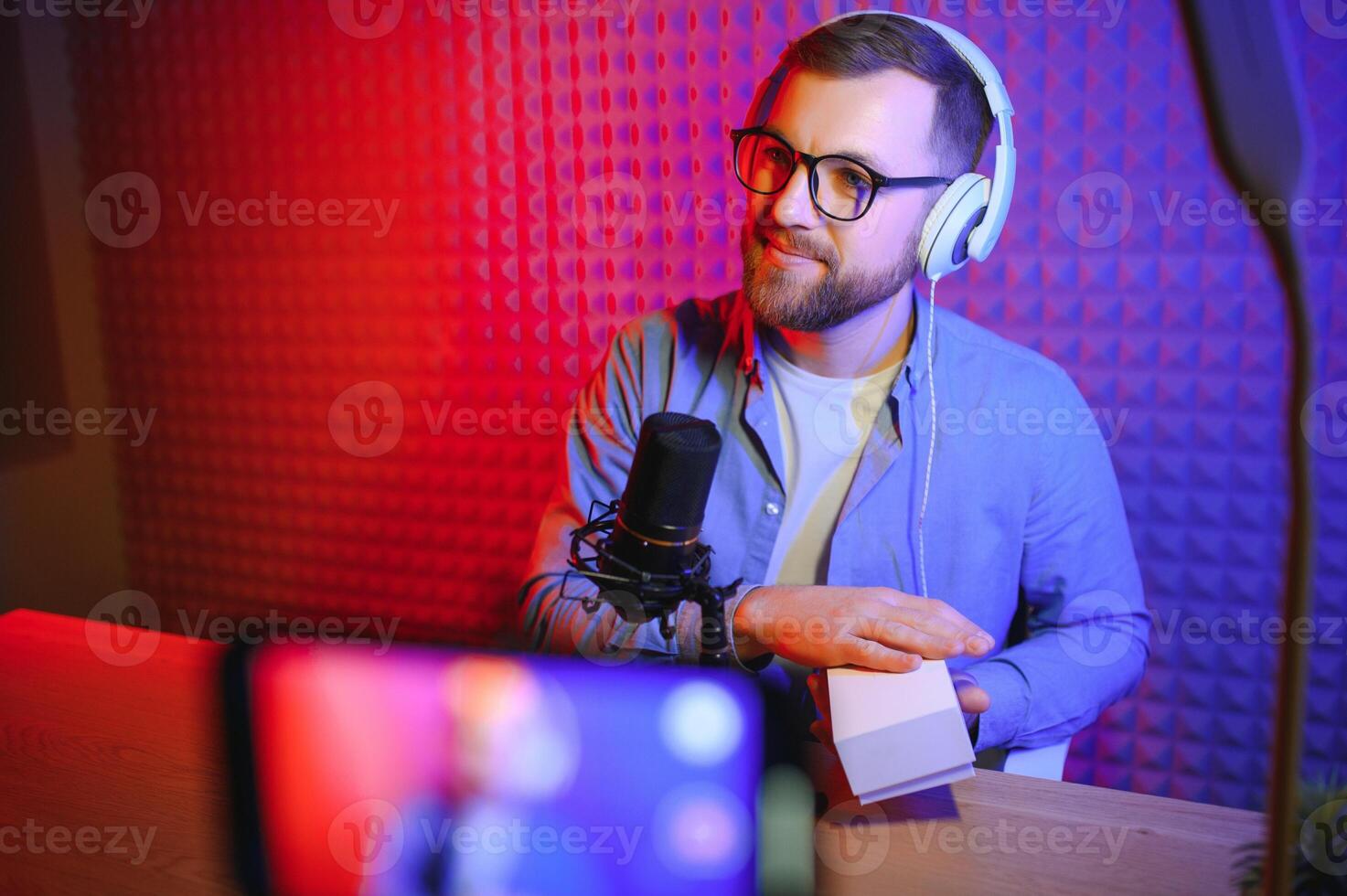 vlogger using smartphone to film podcast in studio. blogger with mobile phone, microphone and headphones filming for social media broadcasting career. photo