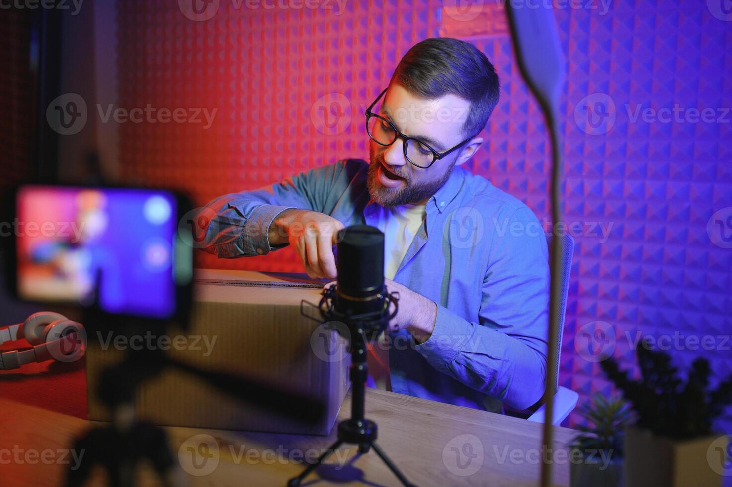 Handsome young man gesturing while unpacking parcel, excited, clenches fists in triumph. Joyful male vlogger. Concept of people and social networks. photo