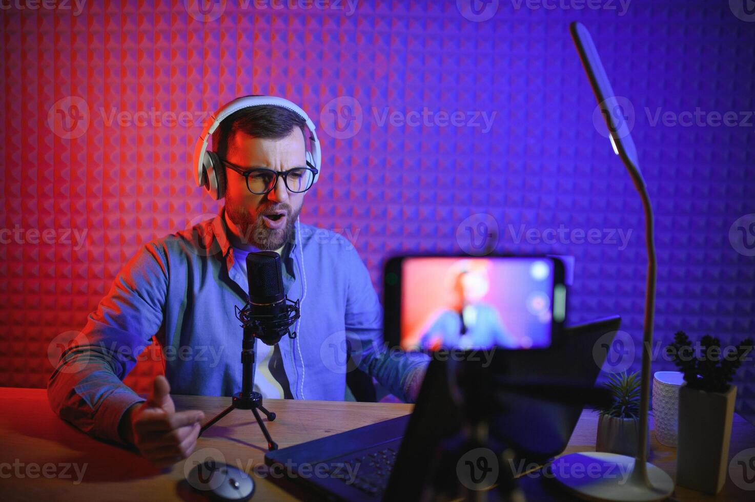 vlogger using smartphone to film podcast in studio. blogger with mobile phone, microphone and headphones filming for social media broadcasting career. photo
