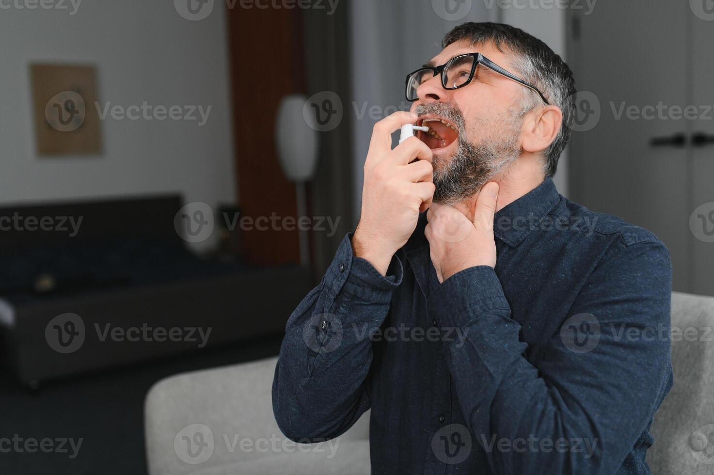 Sick senior man using throat spray at home photo