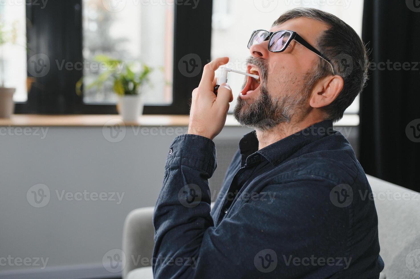 Mature man using an antiseptic throat spray at home photo