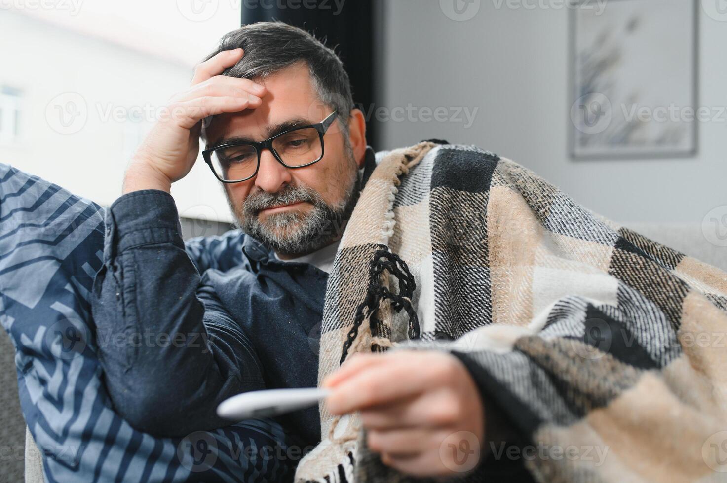 Sick senior man using thermometer checking his temperature suffering from seasonal flu or cold. photo