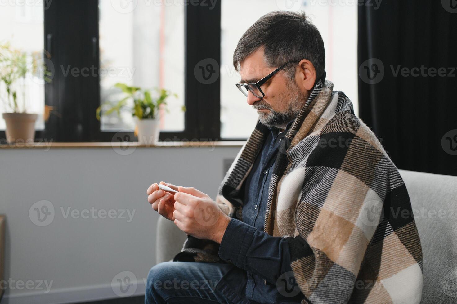 Portrait of sick senior man with thermometer posing at home photo