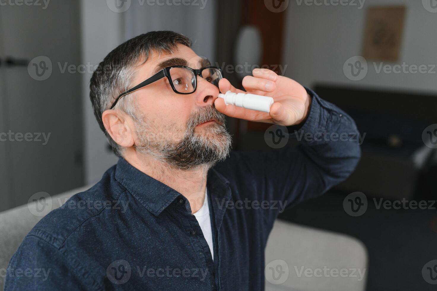 Illness And Sickness. Closeup Of man Feeling Sick Dripping Nasal Drops In Blocked Nose. Portrait male Sprays Cold And Sinus Medicine In Runny Nose. Sinusitis treatment photo