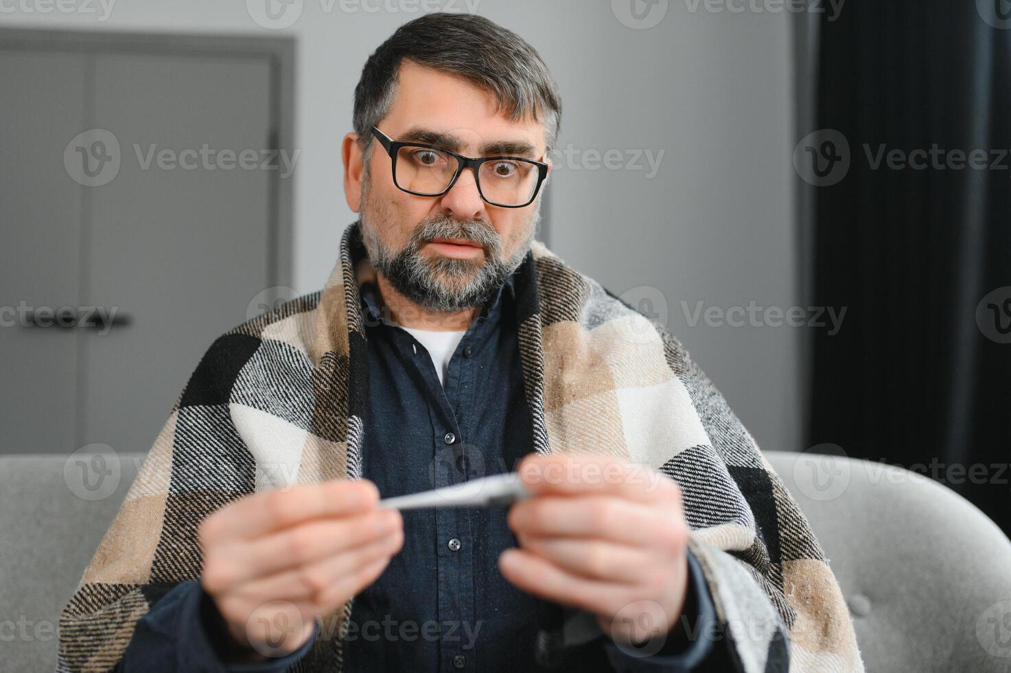 Sick senior man using thermometer checking his temperature suffering from seasonal flu or cold. photo