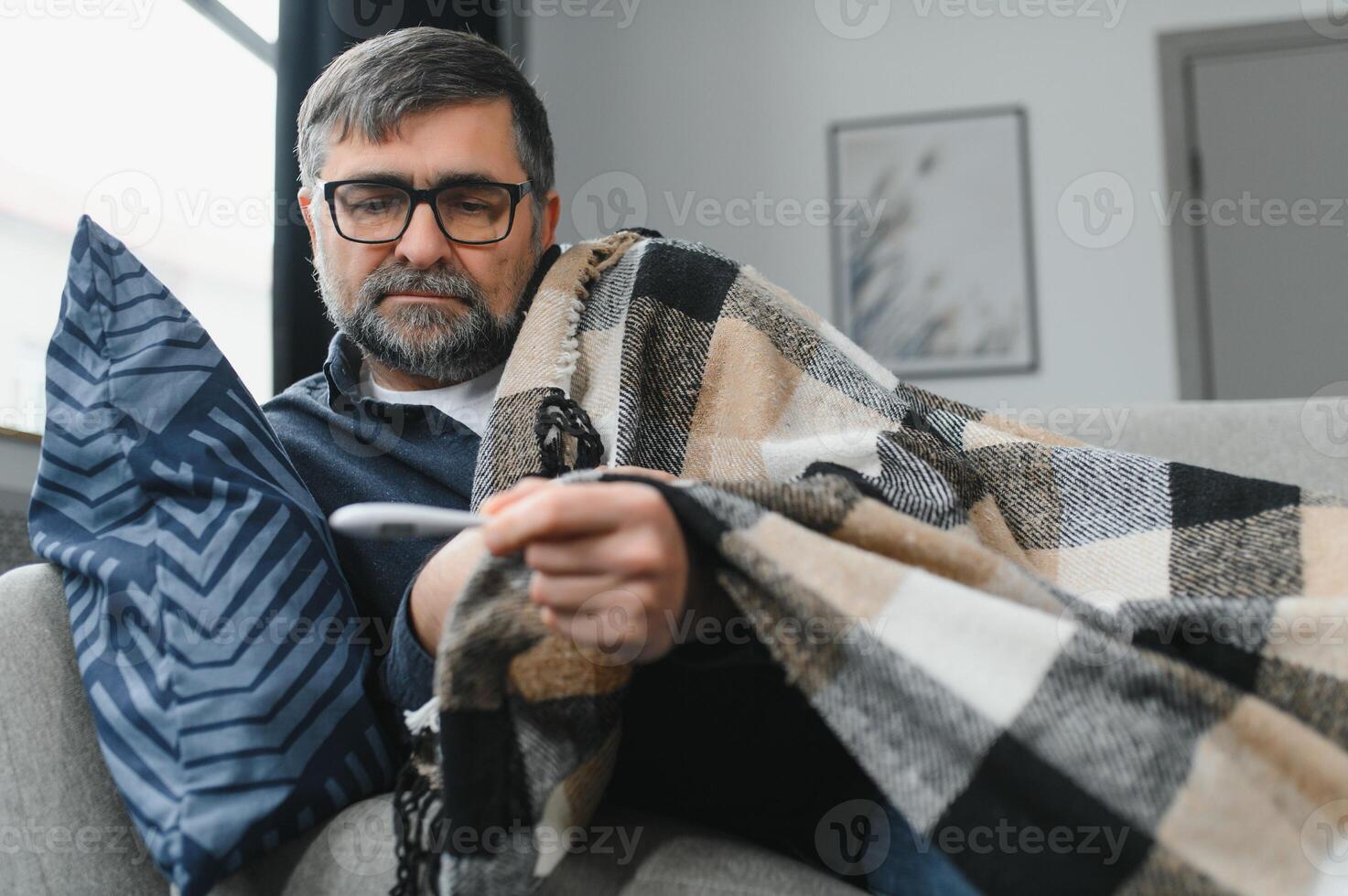 Sick senior man using thermometer checking his temperature suffering from seasonal flu or cold. photo